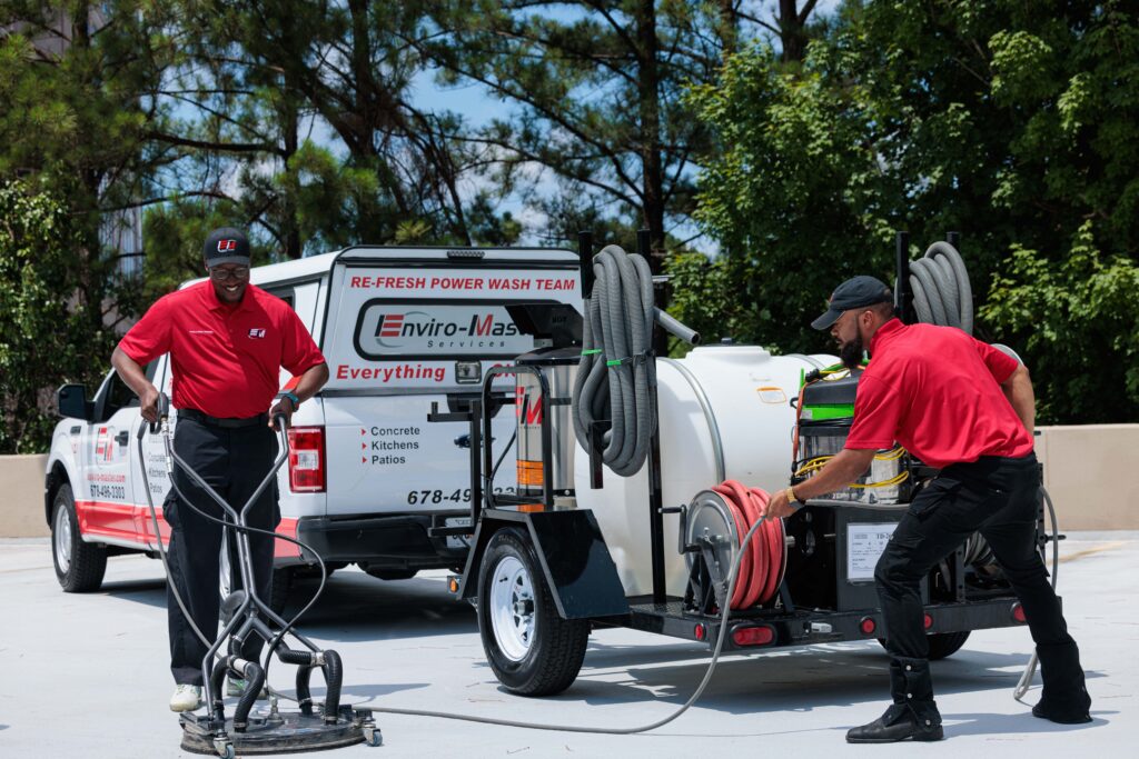 Two Enviro-master employees using a pressure washer in a parking lot