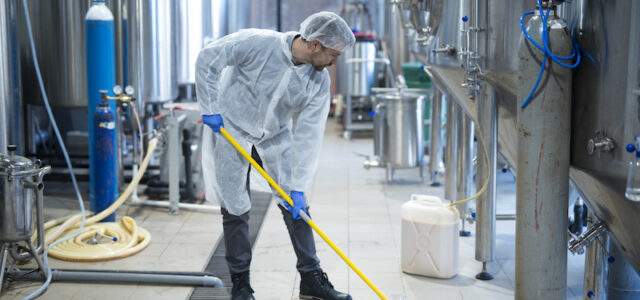 Professional industrial cleaner in protective uniform cleaning floor of food processing plant. Cleaning services.