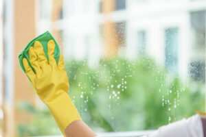 Woman housekeeper cleaning the double pane window with green cloth.