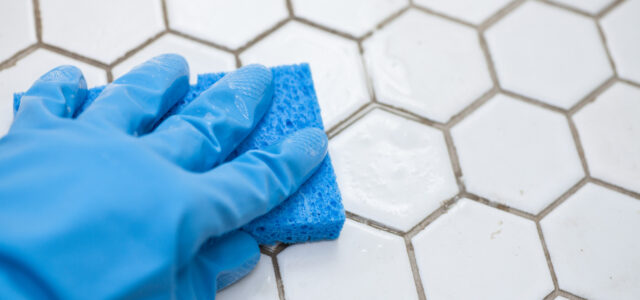 a person wearing blue gloves holds a sponge cleaning a white tile floor