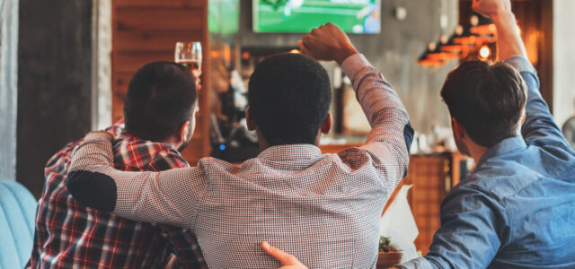 Three men watching football on TV in sport bar, back view