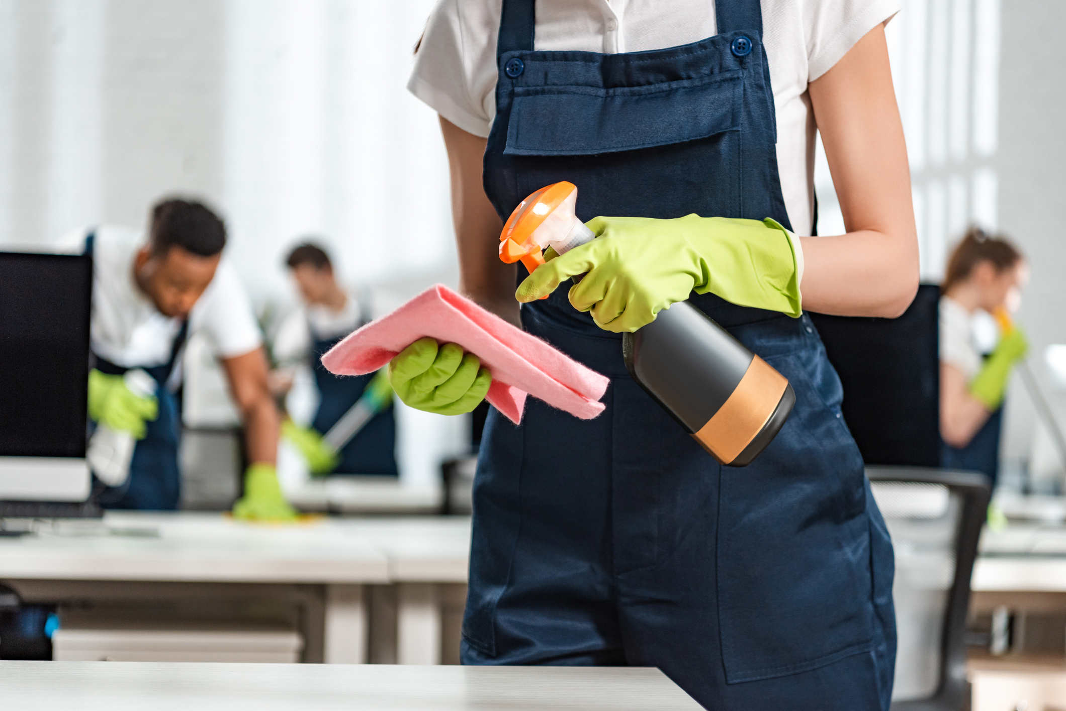 cropped view of cleaner in uniform spraying detergent on rag