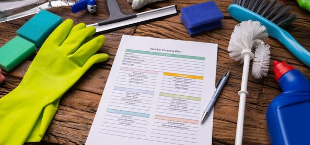 Close-up Of Various Cleaning Products Around Weekly Cleaning Plan Form With Pen