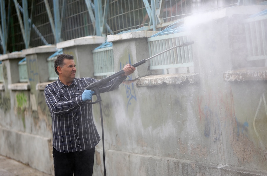 A cleaner is cleaning graffiti from the outer side of a wall of a school.