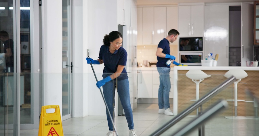 Woman mopping floors in an office building, man wiping off counters. 