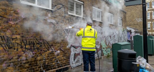 A worker cleaning graffiti off a building with a jet power wash.