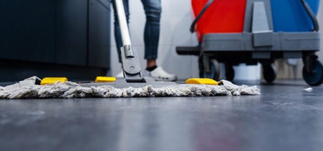 A person mops a floor while standing next to one red bucket and one blue bucket.