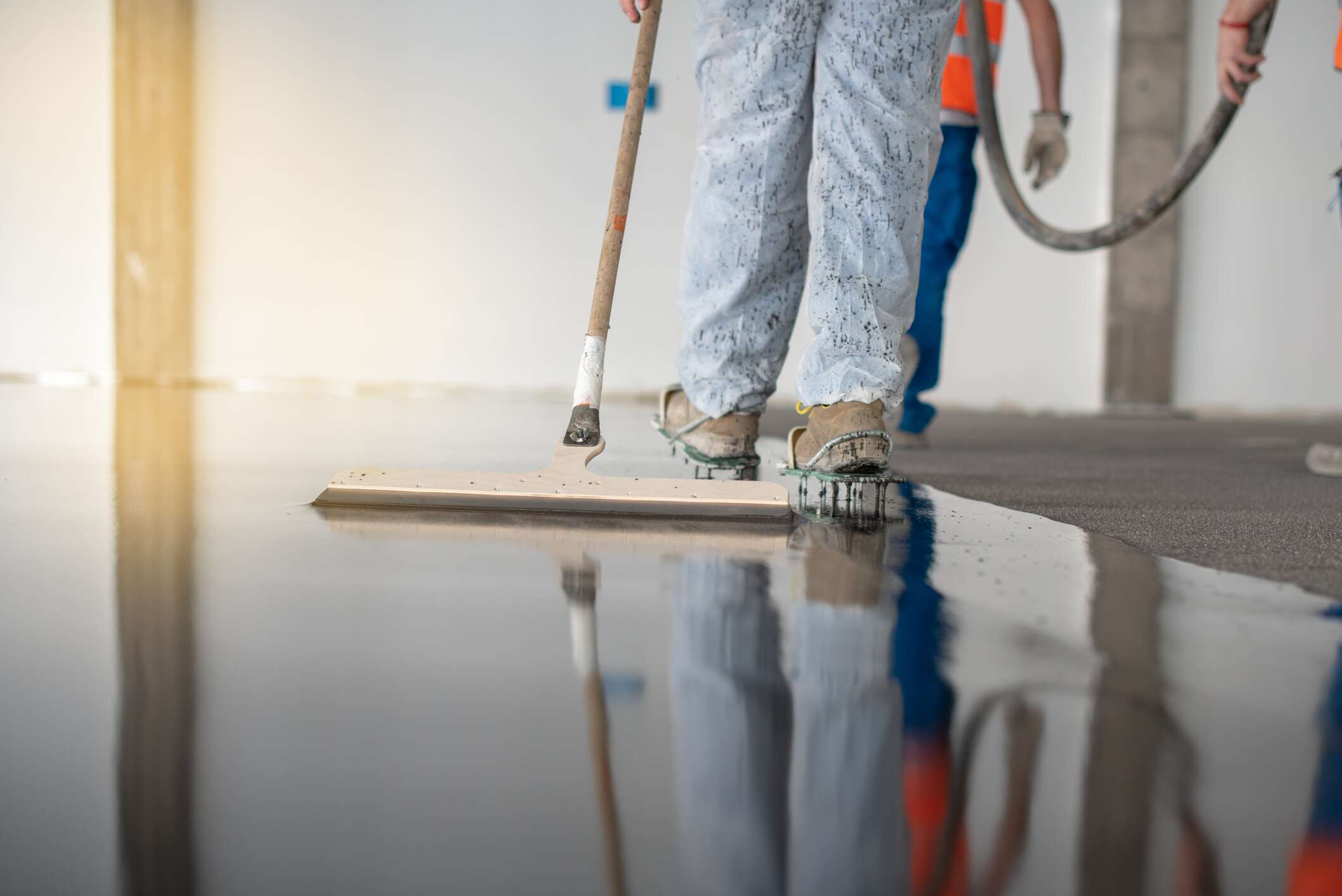 A worker finishes a wet concrete floor for an industrial building.