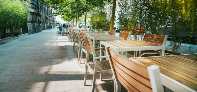 Outdoor restaurant tables in front of urban greenery.
