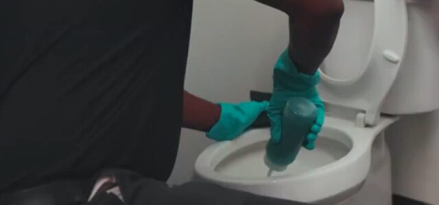An Enviro-Master professional cleans a toilet in a commercial bathroom.