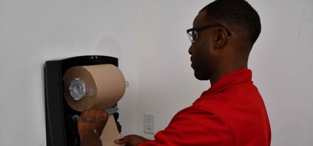 An Enviro-Master technician replaces a paper towel roll in a paper towel dispenser.
